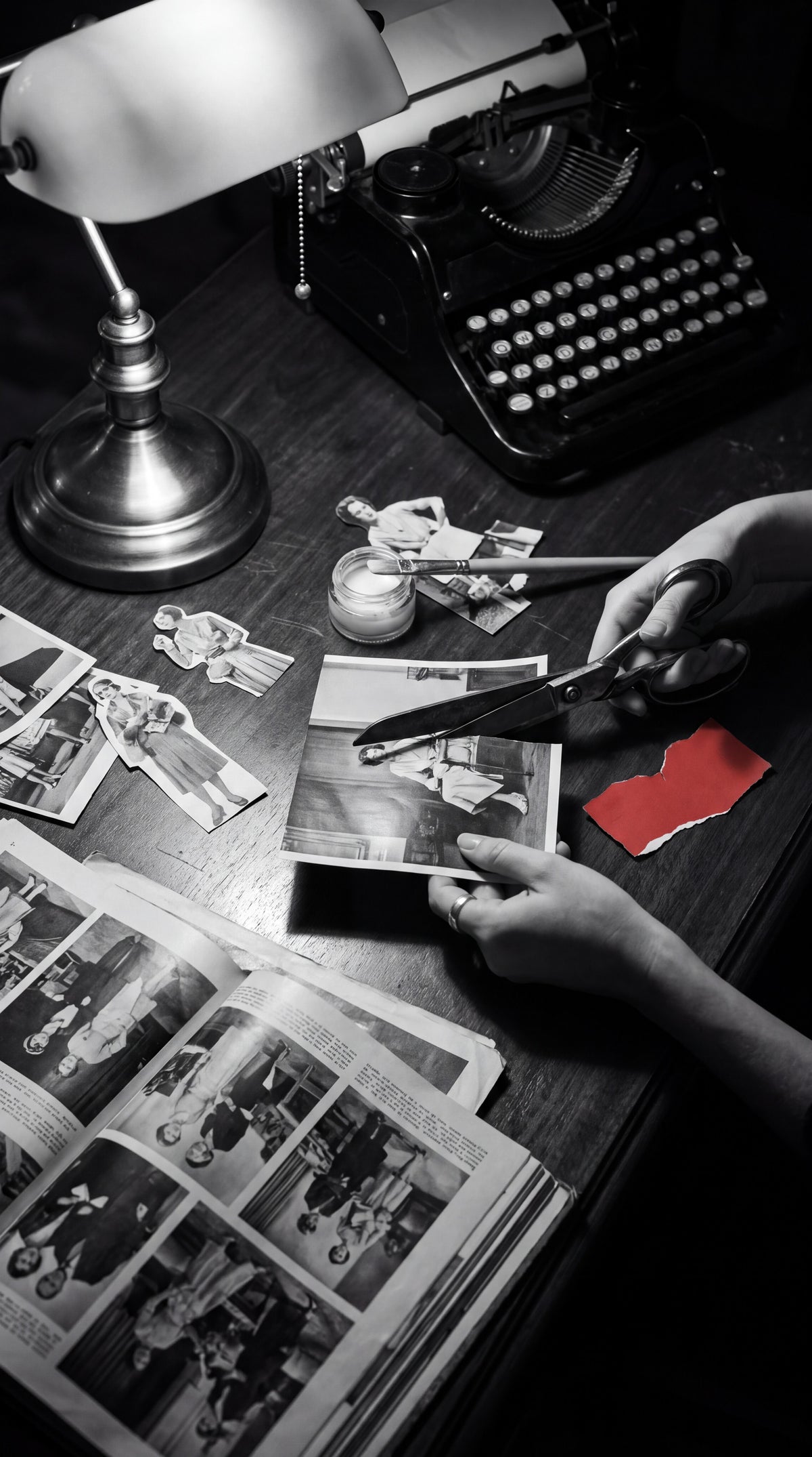 Hands cutting old photographs at a work table, a typewriter and a lamp behind, one scrap of red paper